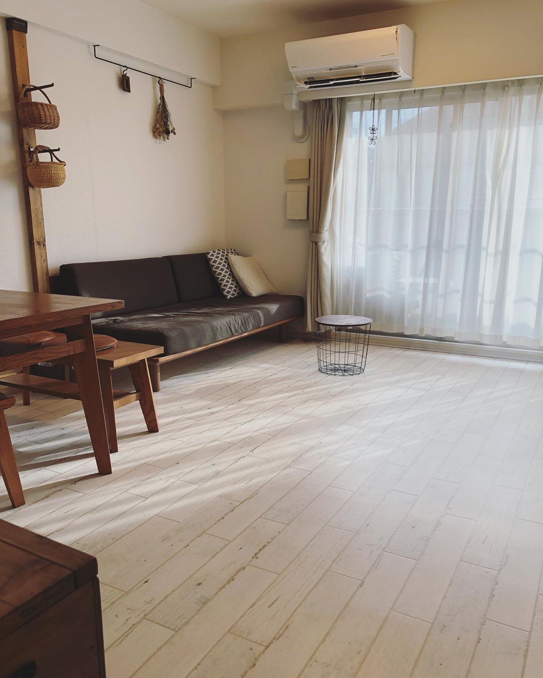 明るい木目（白のホワイトウォッシュ風）のクッションフロアをリビングに敷いた実例。木製家具やブラウンのソファと調和し、やわらかな光に満ちたナチュラルな空間に仕上がっている。