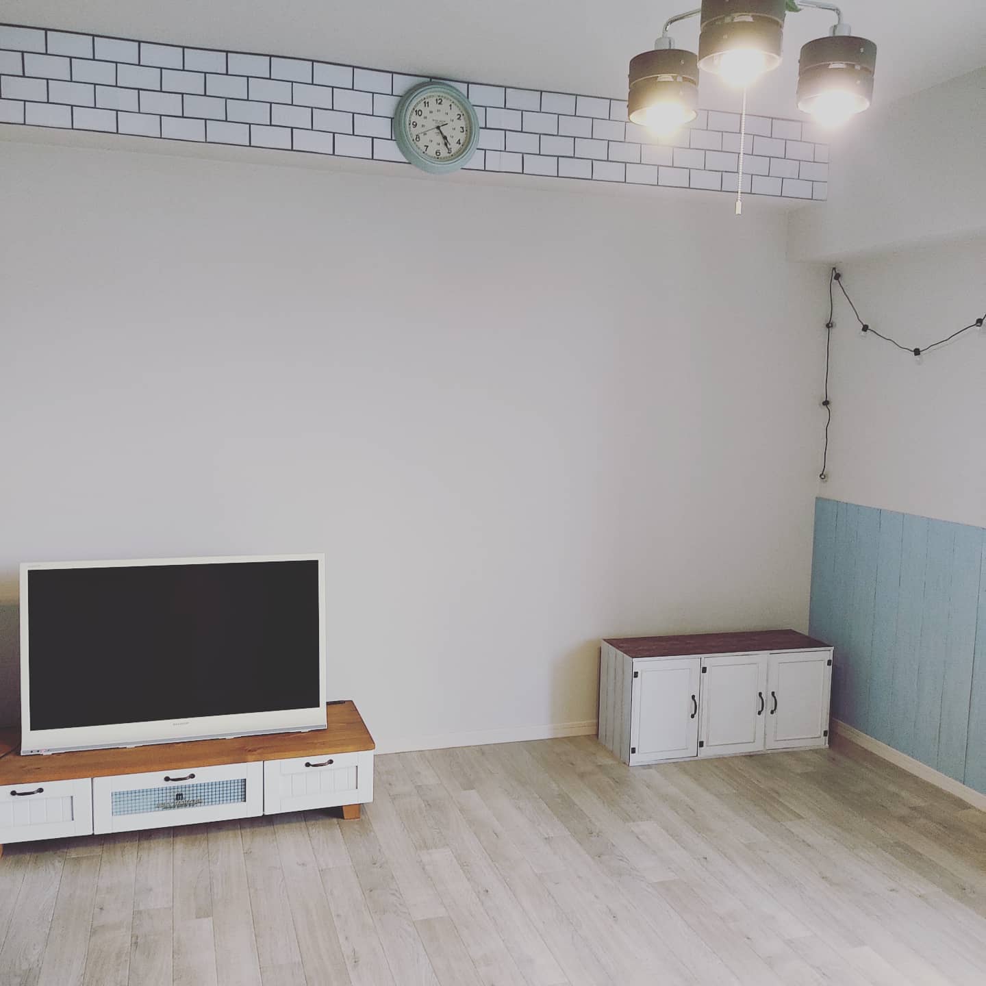 明るい木目のクッションフロアをリビングに敷いた実例。ホワイト家具やブルーのアクセントウォールと調和し、爽やかで開放感のある空間に仕上がっている。