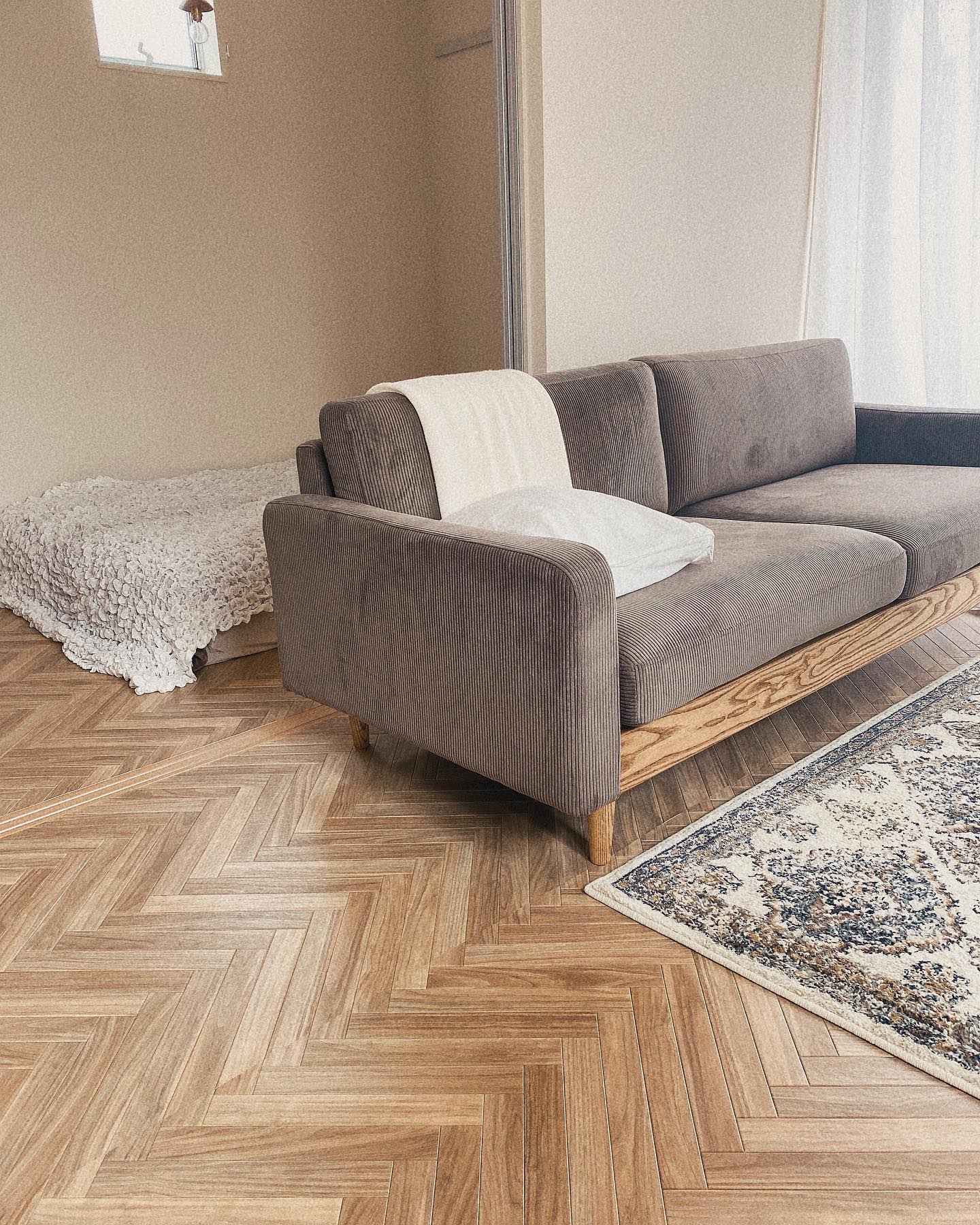 ナチュラルなブラウン系のヘリンボーン柄クッションフロアをリビングに敷いた実例。ブラウンソファとラグが調和し、あたたかみのある上品な空間に仕上がっている。