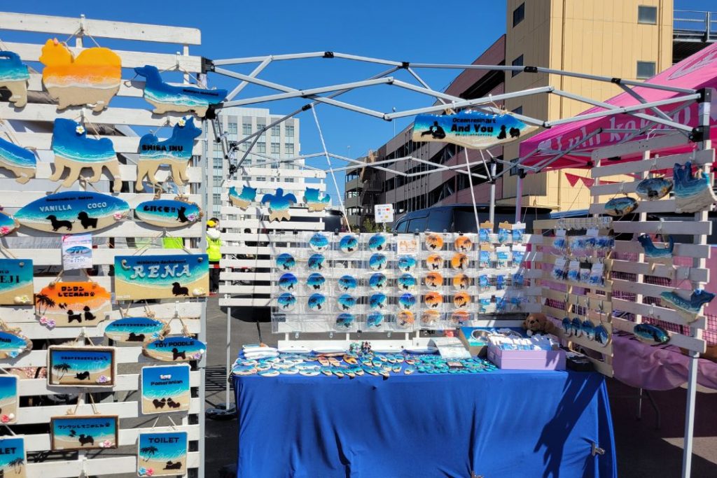 WANDARAKE MARCHÉの犬雑貨販売ブース:犬のシルエットや肉球、海をモチーフにしたカラフルなキーホルダーやネームプレートが多数展示されている。柴犬やダックスフンドなど様々な犬種のシルエットが見られる。