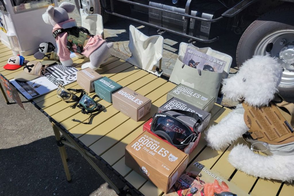 WANDARAKE MARCHÉの犬用ゴーグル専門店:テーブルには、様々なデザインと色の犬用ゴーグルが箱に入って並べられている。犬のぬいぐるみ2体がゴーグルや洋服を着用してディスプレイされている。
