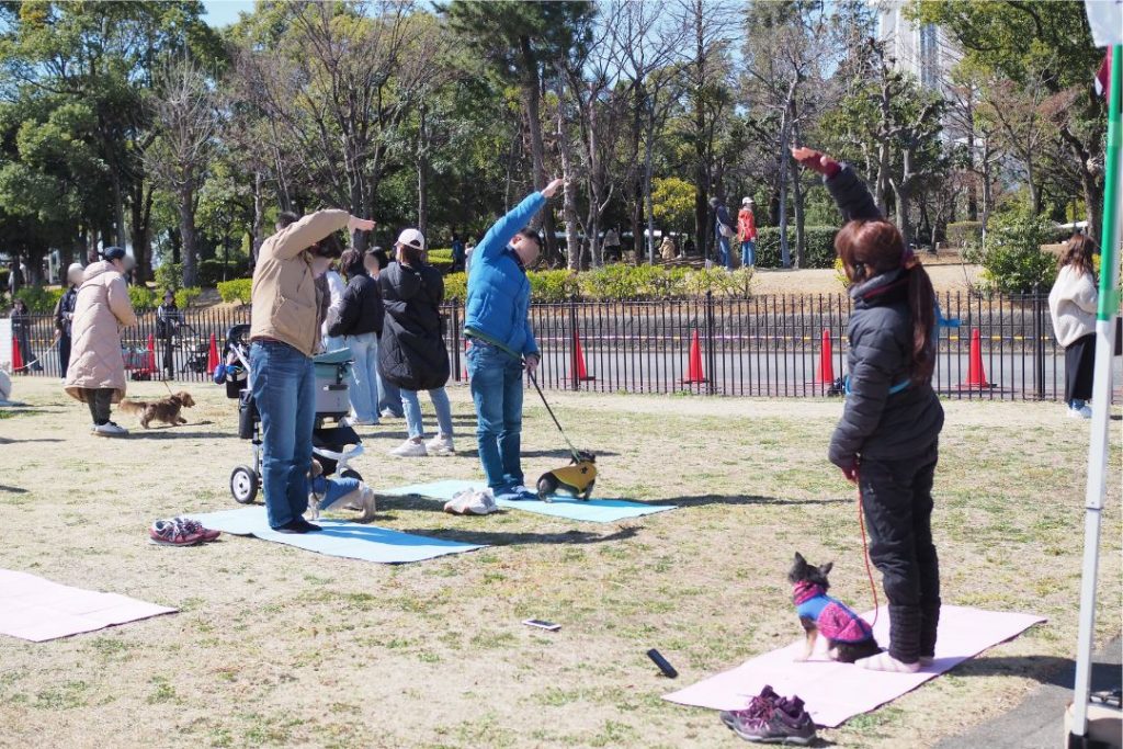 WANDARAKE MARCHÉのドッグヨガ体験:飼い主と犬が一緒にヨガマットの上でポーズを取る様子。青空の下、開放的な雰囲気の中でイベントを楽しむ人々。
提案2:参加者と犬の様子を具体的に描写したaltテキスト