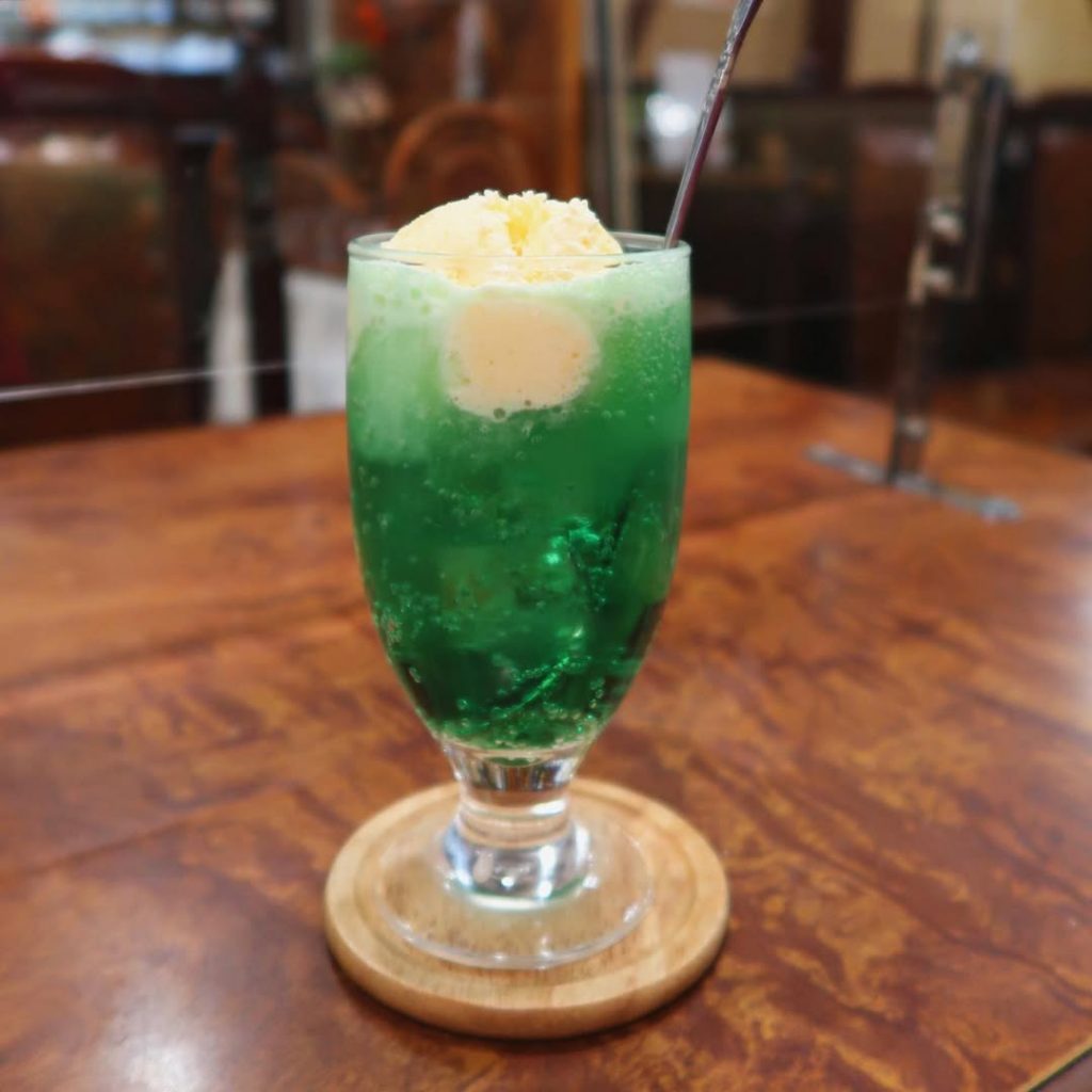 昭和喫茶の定番メニュー、バニラアイスがのったクリームソーダ|木目調テーブルの上に置かれた鮮やかな緑の一杯