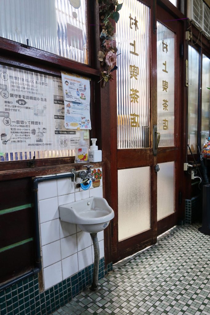 喫茶むらかみの店内入口付近、小さな洗面台とガラス扉のレトロな空間|昭和の喫茶店らしい佇まいと床タイル