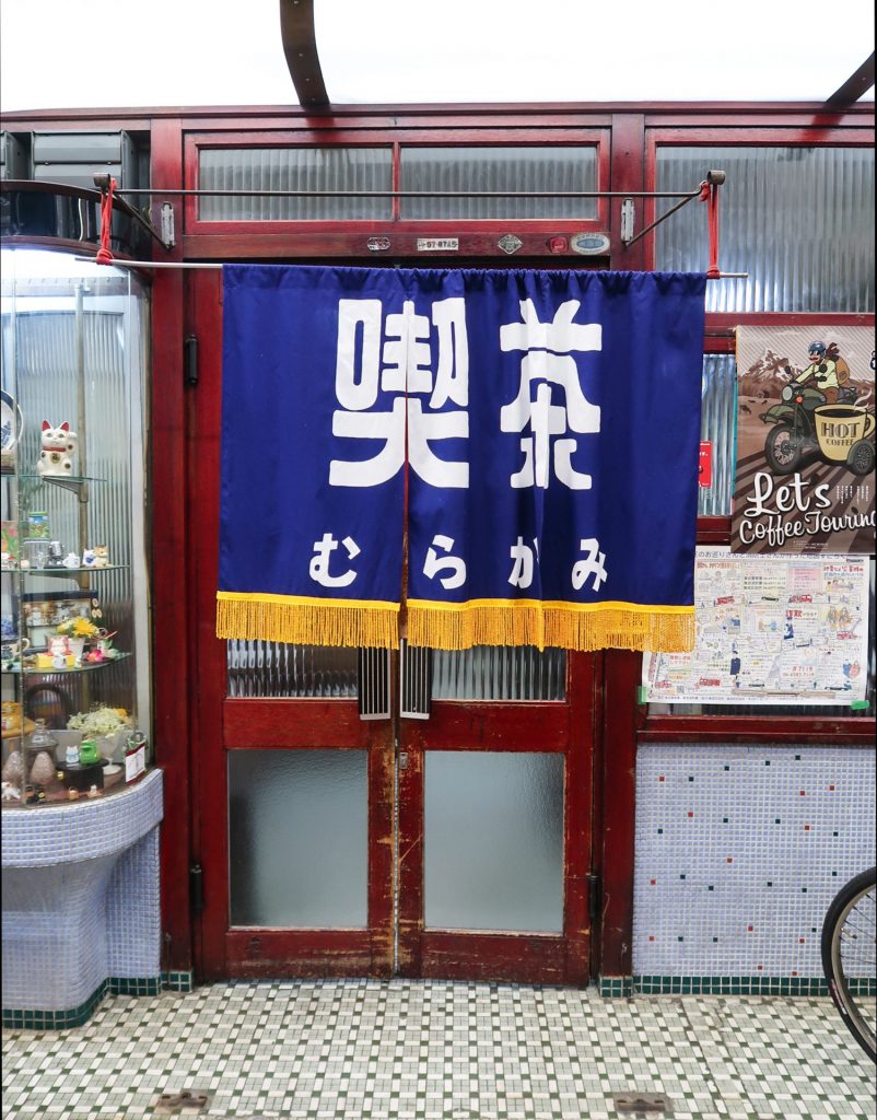 青い暖簾が印象的な喫茶むらかみの店先|レトロなガラス戸とモザイクタイルの床が懐かしい雰囲気を演出