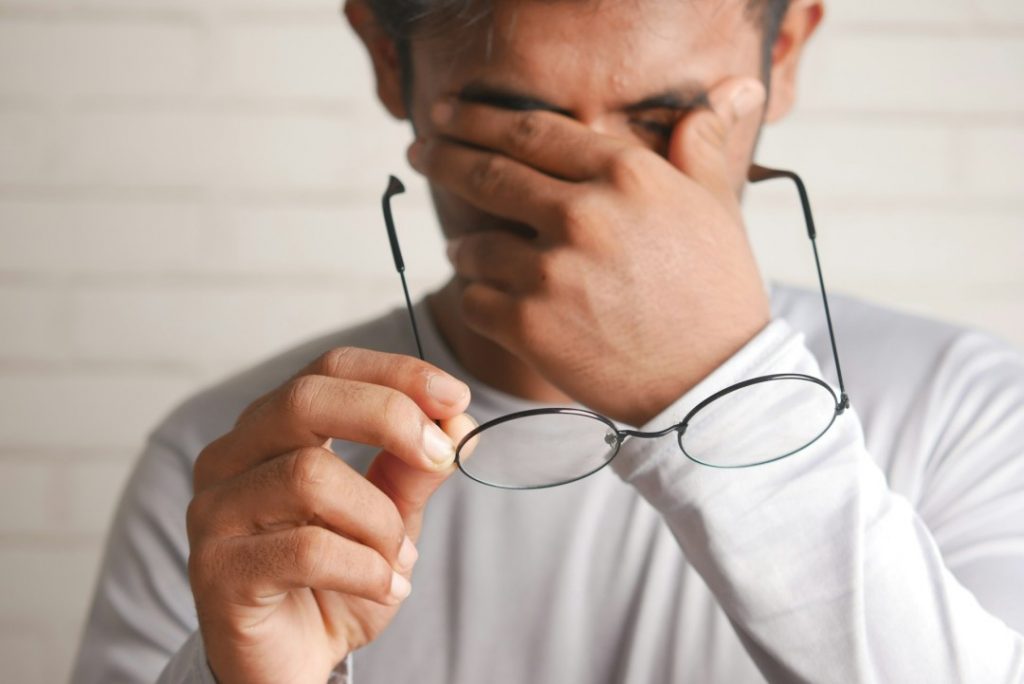 眼鏡を外し、目を抑える男性