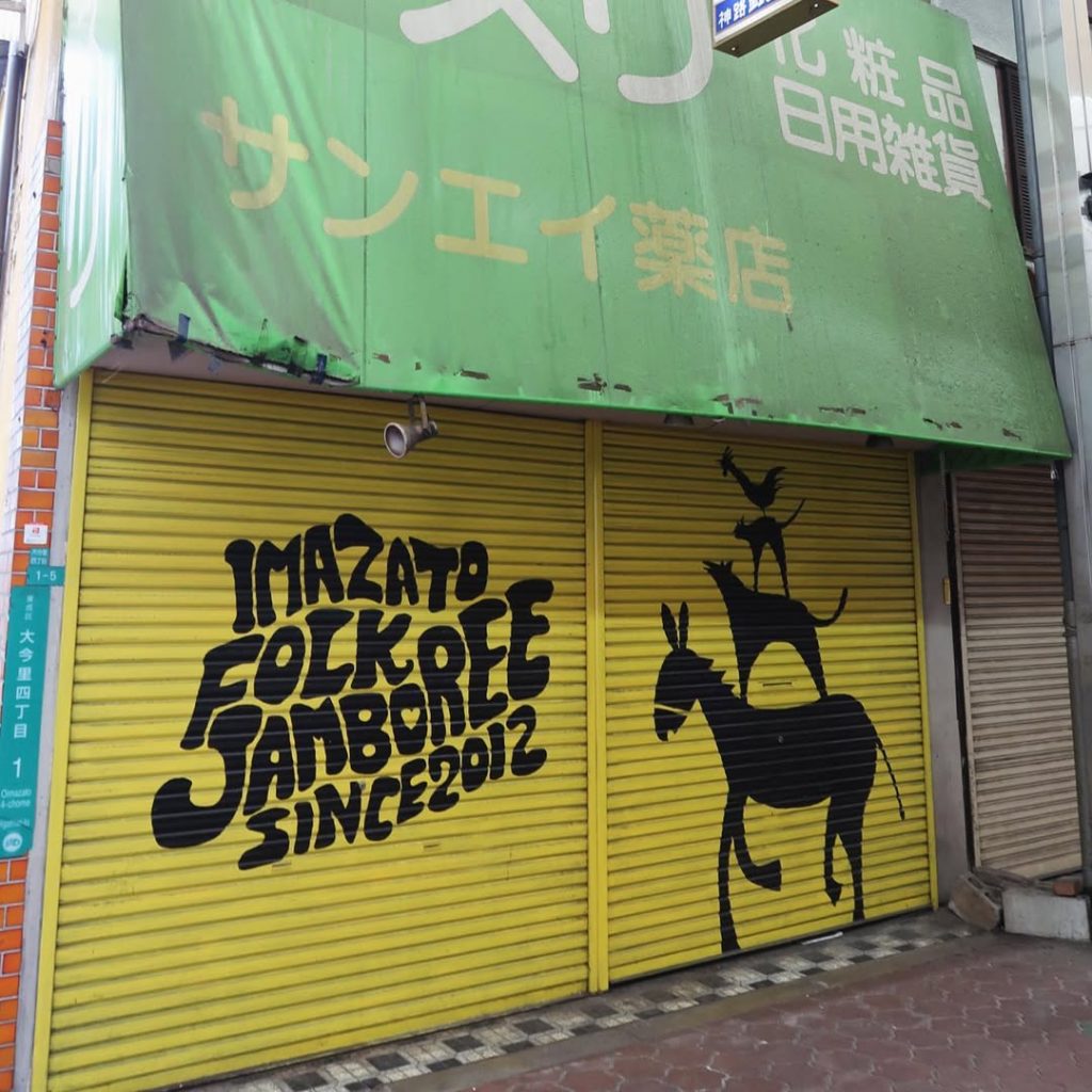 ブレーメンの音楽隊を描いた黄色いシャッターが印象的な今里商店街の一角|サンエイ薬店の看板とレトロな外観