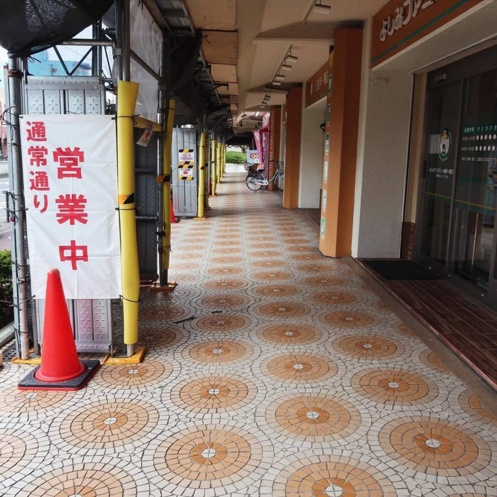 オレンジと白の円形タイルが並ぶ大阪のアーケード商店街の床風景|足元に広がる幾何学模様と営業中の幕が印象的