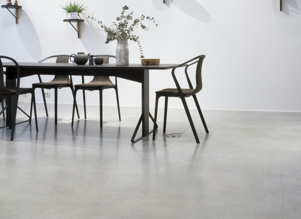 モルタル調の床が映えるシンプルモダンなダイニング空間。クールなグレートーンの床とブラックチェアが洗練された印象を演出