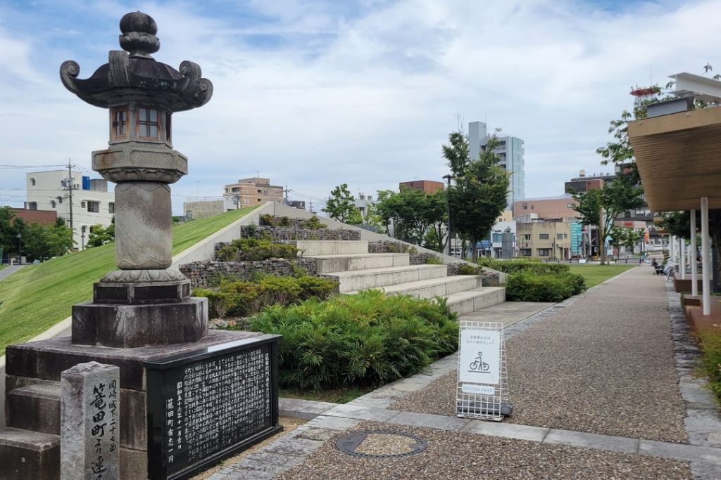 寛政10年に建立された常夜灯と、階段状の植栽と芝生が整備された岡崎市の籠田公園の風景。