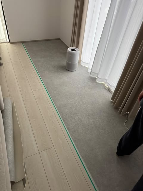 ラグリエのペットマット〈モルタル〉をリビングのフローリング上に敷き込み中。吸着滑り止めテープで位置を調整しながらDIY施工。