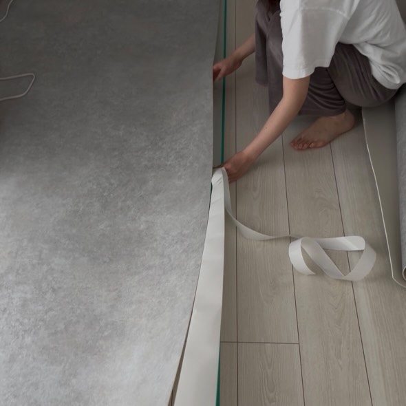 ラグリエのペットマット〈モルタル〉を吸着滑り止めテープで固定している様子。フローリングに貼らずにズレを防ぐ安心の床DIY。