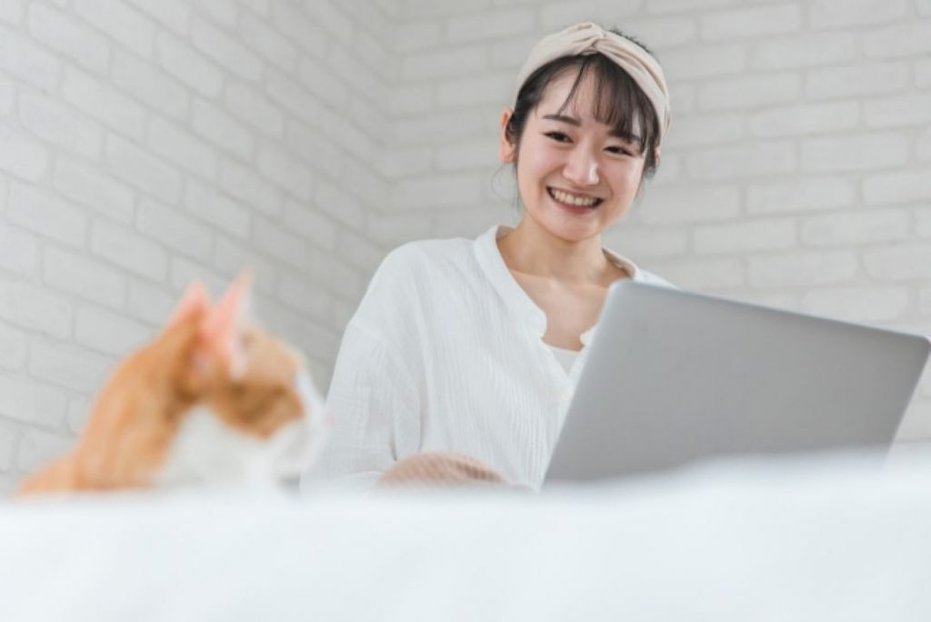 猫をそばに、ノートパソコンでSNSを楽しむ女性。愛猫の姿を共有する前に守るべき撮影マナーを考える。