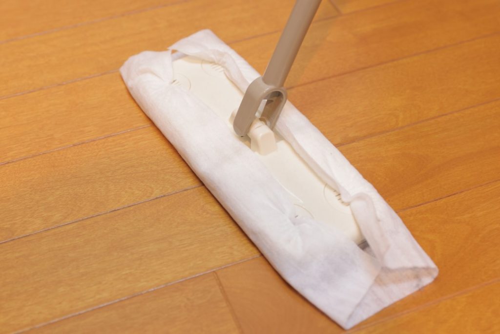 木目調のクッションフロアをドライシート付きフロアワイパーで掃除している様子。静電気で舞い上がるホコリを効果的に取り除く床掃除方法。