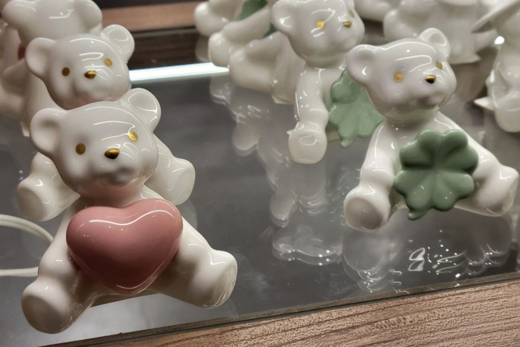 ノリタケの森ショップに並ぶ陶磁器製のクマの置物で、ピンクのハートとグリーンのクローバーを持ったデザイン。