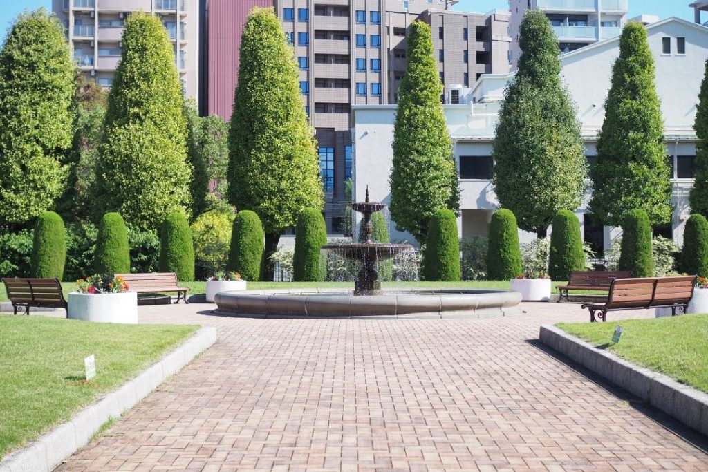 ノリタケの森の中心にある噴水と整然と並ぶ円錐形の並木を撮影した庭園風景。