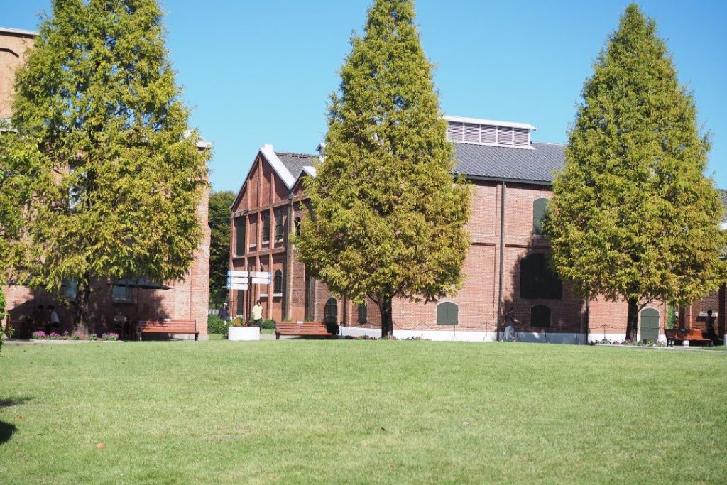 芝生広場越しに見えるノリタケの森の赤レンガ建物と整えられた並木。