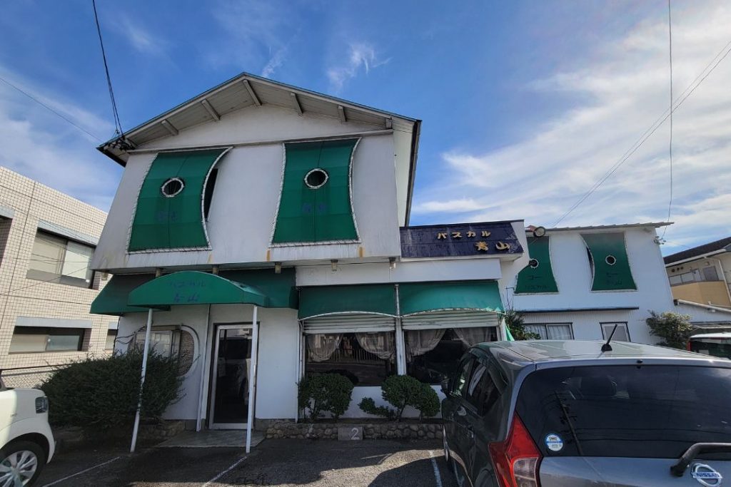 喫茶パスカル青山の外観。緑のオーニングと丸窓が印象的な白い建物。