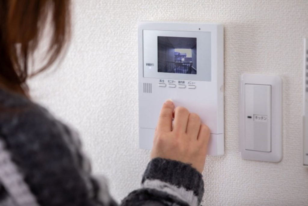 ペット可物件での騒音トラブルを避けるため、インターホンで来客対応をして周囲への配慮をする女性のイメージ。日常のマナーでご近所トラブルを未然に防ぐことを示す写真