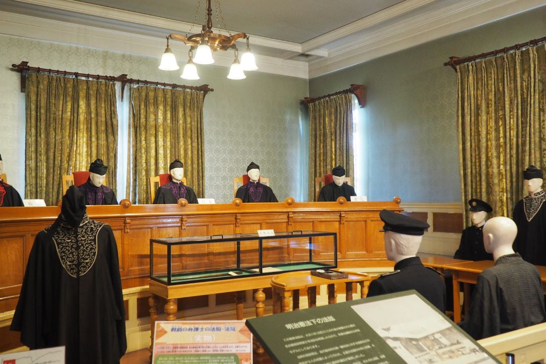 名古屋市市政資料館の模擬法廷展示。裁判官や書記を模した人形が並び、当時の法廷の様子が再現されている。