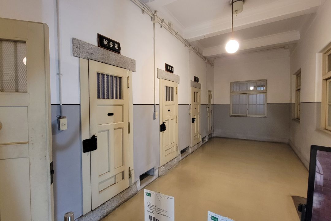 名古屋市市政資料館の旧留置場エリア。分厚い木製扉が並び、番号札や鉄格子などが当時のまま保存されている。