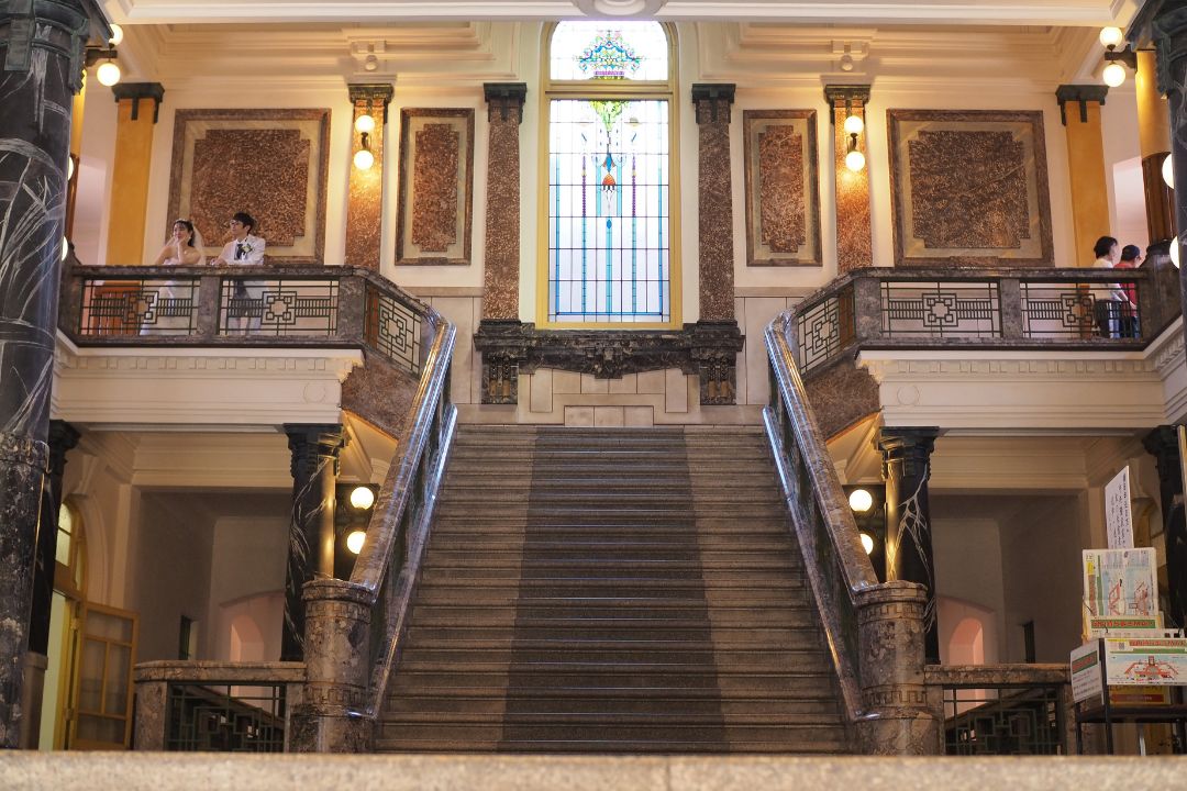 名古屋市市政資料館の中央階段ホール。大階段の奥に大きなステンドグラスが浮かぶクラシックな内装。