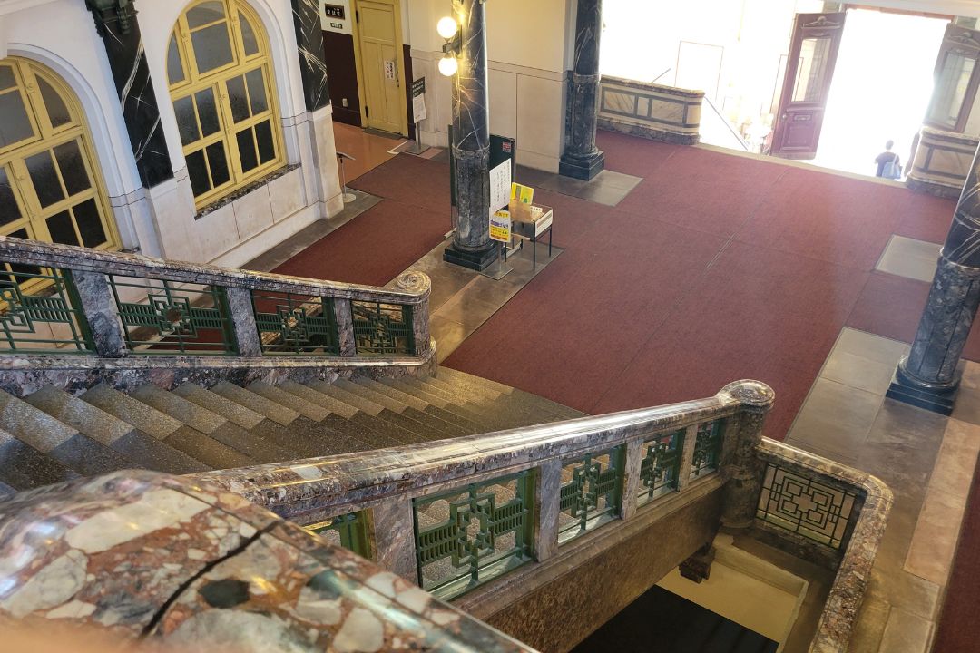 名古屋市市政資料館の中央階段を上から見下ろした構図。広いエントランスと大理石手すりが見える内観。