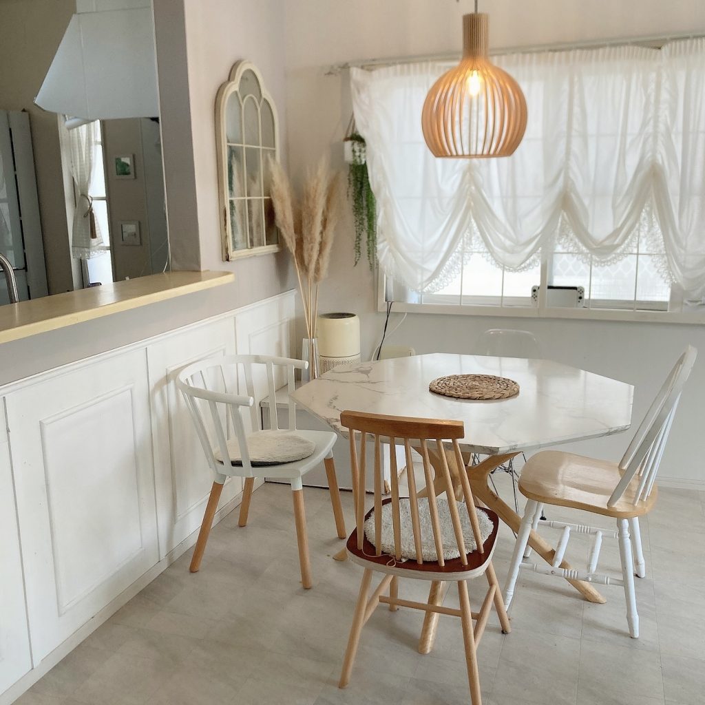 グレー系の床と木製チェアを組み合わせた明るいダイニング。白いカーテンやラタン調の照明が柔らかい雰囲気をつくるナチュラルインテリア。