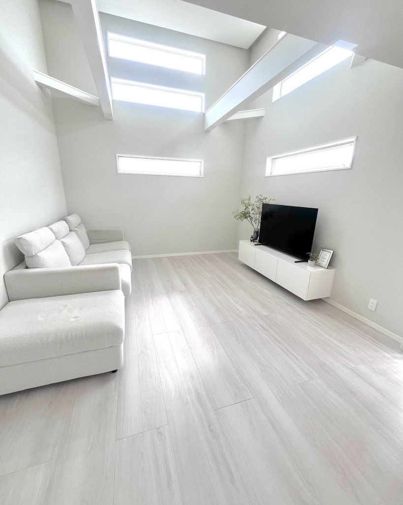 リビング全体に白木調の床が広がる入居時の状態。白いソファとテレビボードが置かれた、明るくシンプルなビフォー写真。