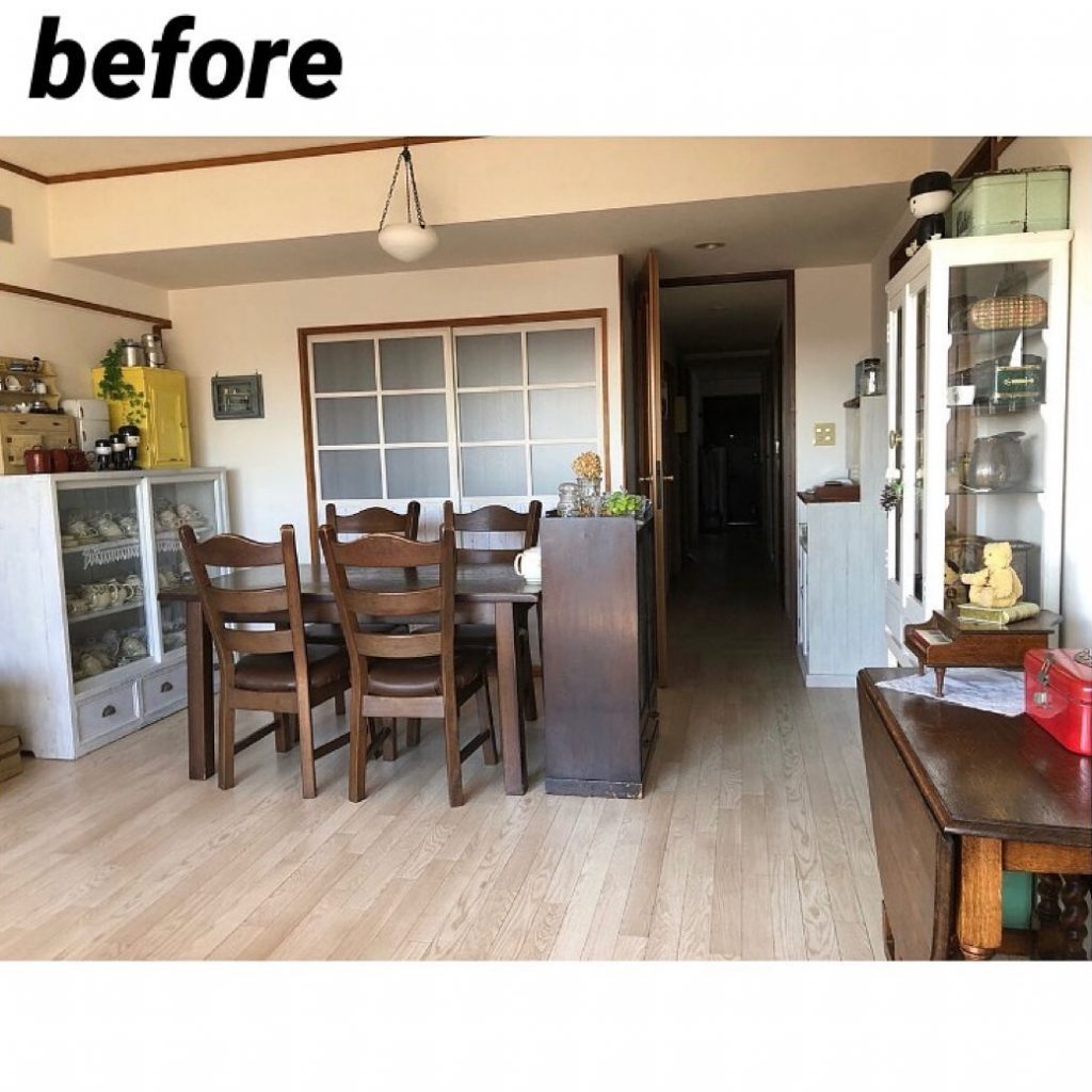 古いフローリングのダイニング。木製テーブルと椅子、食器棚などが置かれた生活感のある室内が写っている。