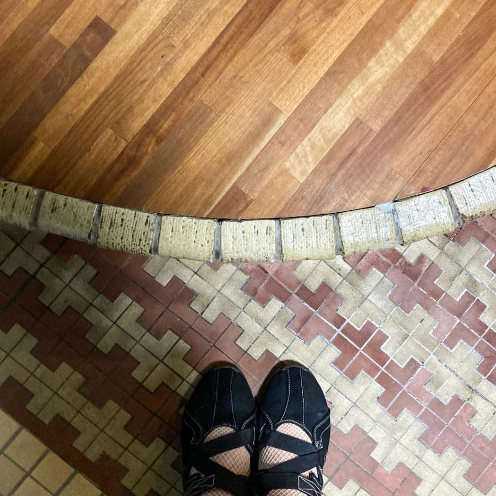 美香茶楼の玄関土間と上がり框の境目。幾何学模様のタイル床から、丸く縁取られた段差のタイルと木床へと切り替わる意匠が特徴的。