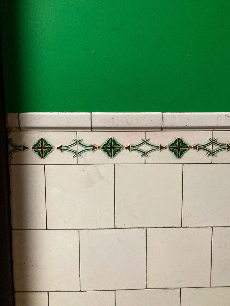 美香茶楼の室内に残る装飾タイル。白い長方形タイルの上部に、緑色の花形モチーフを連続させた縁飾りタイルが配されたレトロな壁面。