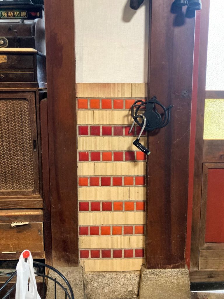 美香茶楼の室内に残る壁際タイル。赤とオレンジの小さなタイルを縦横に組み合わせ、木柱と調和するレトロな装飾が施されている。