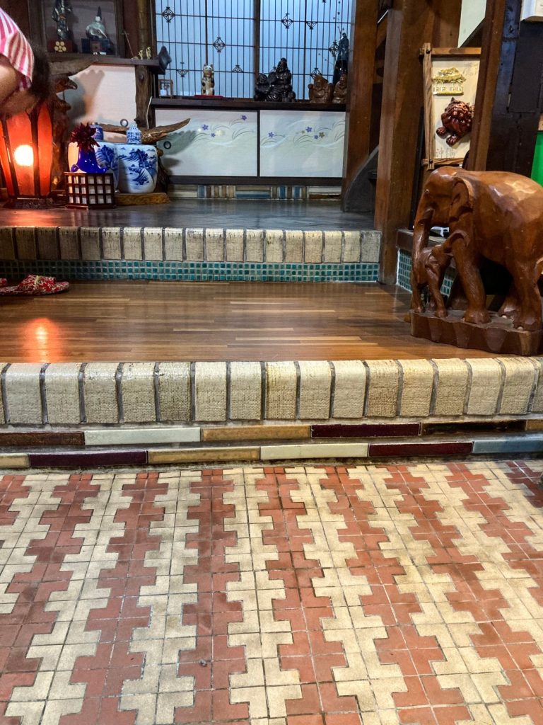 美香茶楼の玄関土間。赤と生成りのタイルを組み合わせた幾何学模様の床が広がり、上がり框にはレトロな長方形タイルがあしらわれている。