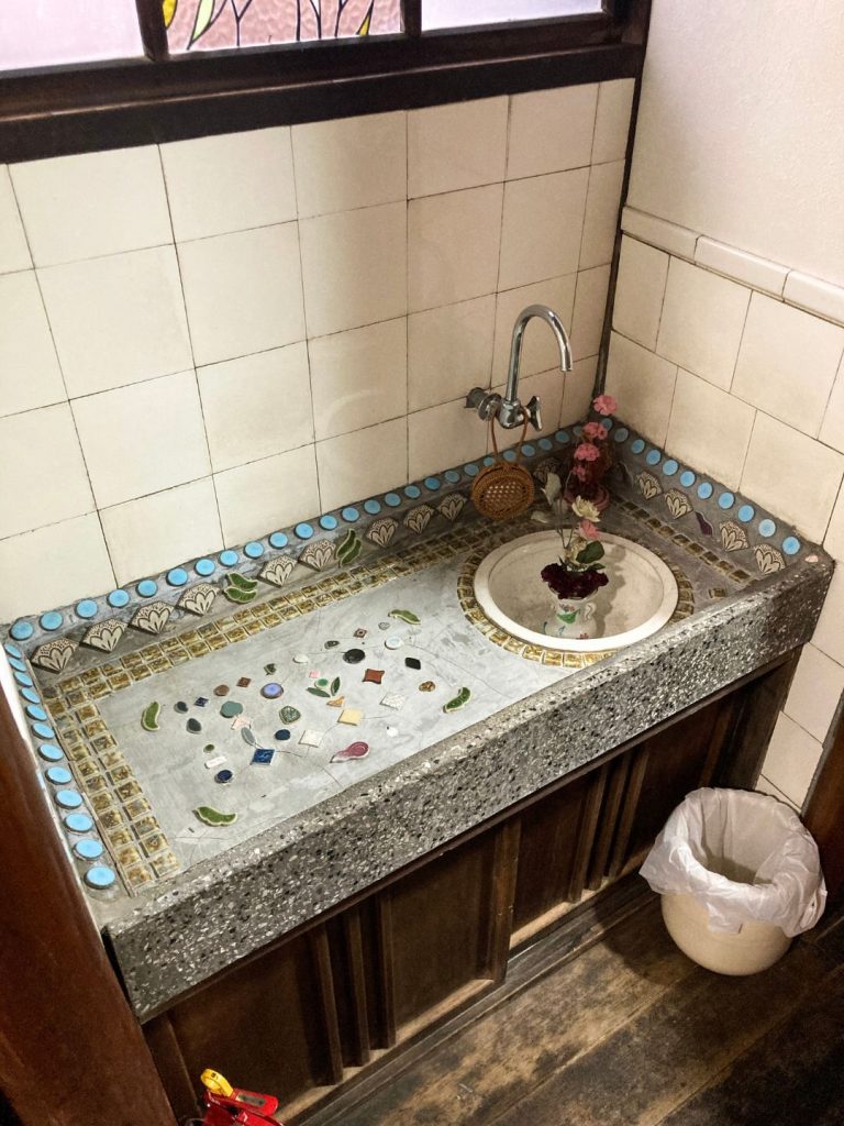 美香茶楼の洗面台。タイル片を散りばめたモザイク調の天板や水色の縁取りタイルが特徴で、レトロな意匠が残る。