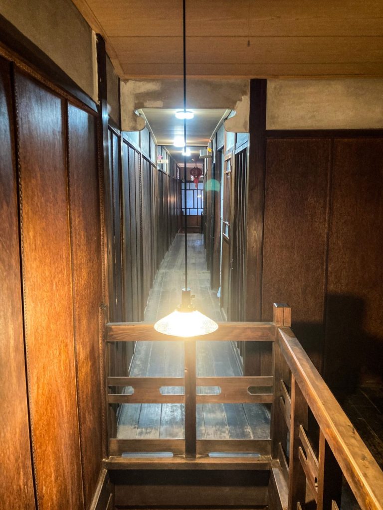 美香茶楼の2階廊下。木板張りの壁と床が続き、吊り下げ照明が柔らかく灯るレトロな通路の佇まい。