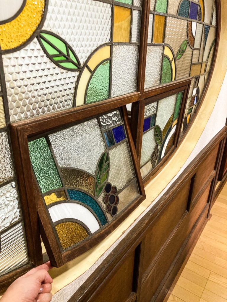 旅館 橋本の香のステンドグラス窓。取り外し可能な小窓を開けて、幾何学模様や植物モチーフの細工を間近で眺めている様子。
