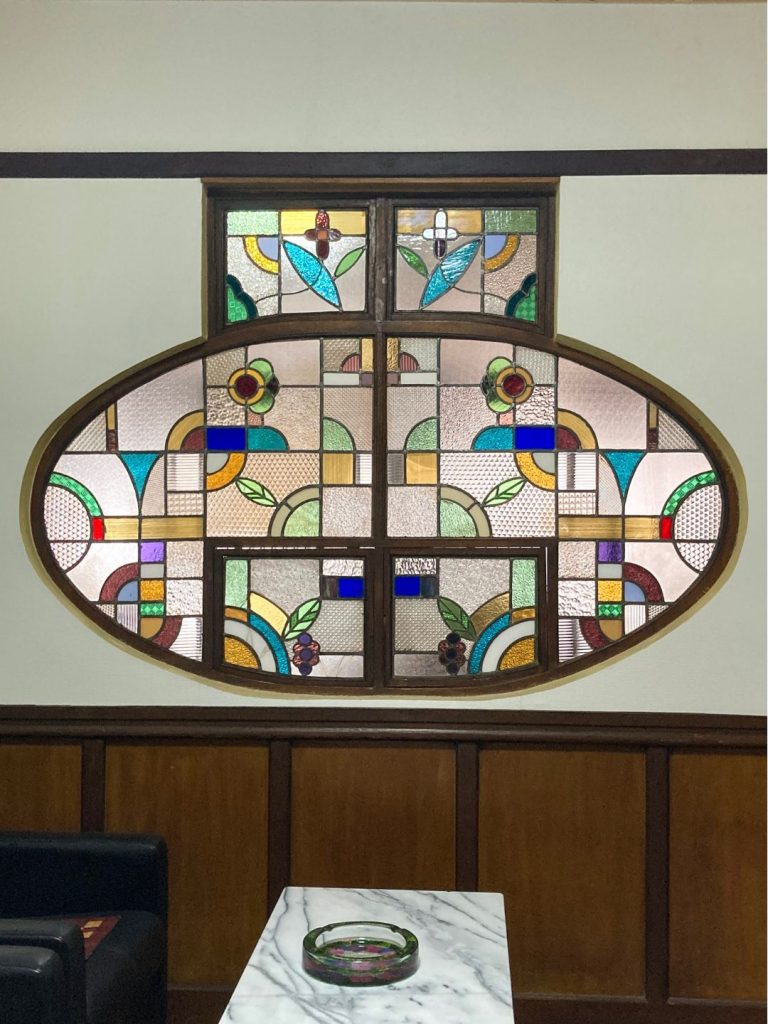 旅館 橋本の香の2階にある楕円形のステンドグラス。幾何学模様と植物モチーフが組み合わさった鮮やかな装飾窓。