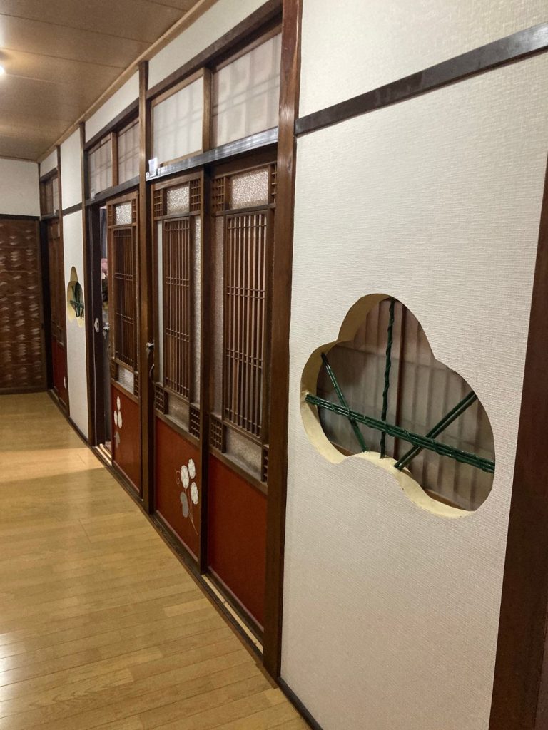 旅館 橋本の香の2階廊下。梅の意匠を施した襖と、葵形の透かし窓が並ぶレトロな和風の空間。