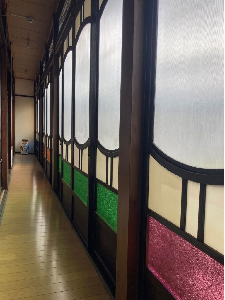 旅館 橋本の香の2階廊下。色ガラスをはめ込んだ建具が並び、レトロな意匠が続く細長い通路。