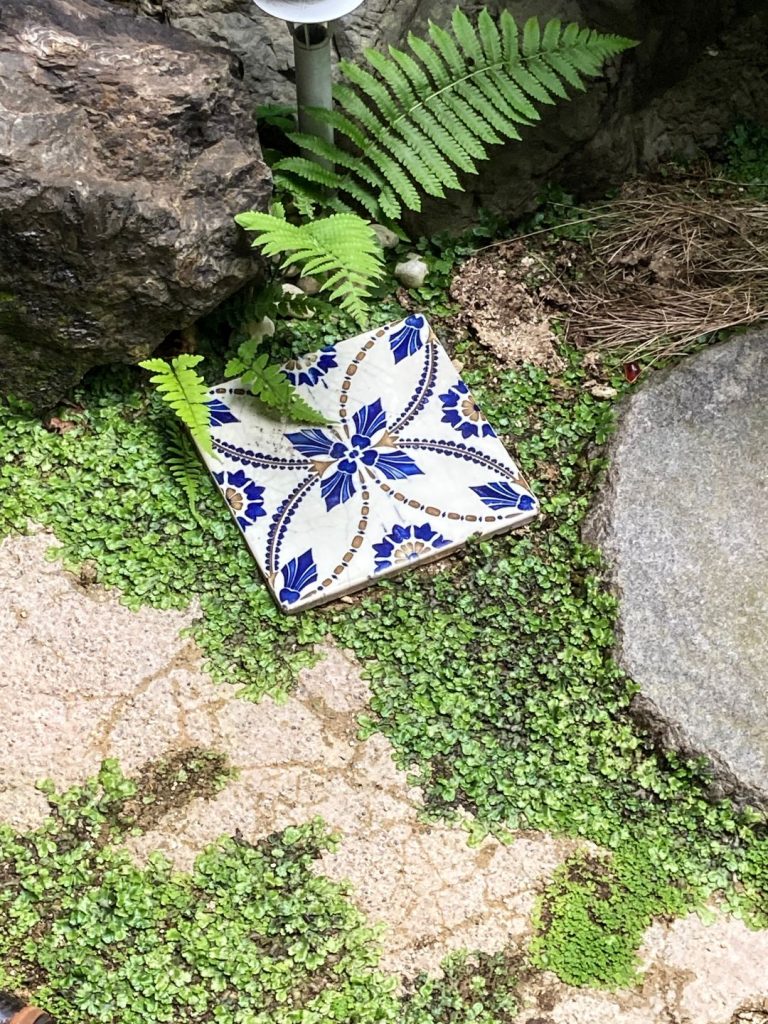 旅館 橋本の香の中庭に置かれた装飾タイル。青い花模様が描かれたタイルが苔むした地面と石の間にさりげなく佇む。