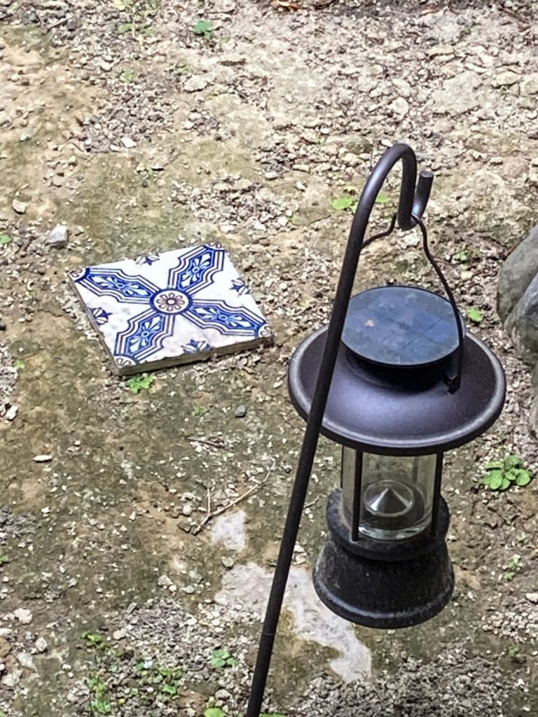 旅館 橋本の香の中庭に置かれた装飾タイルとランタン。青い模様のタイルが土庭の一角で静かに存在感を放つ。