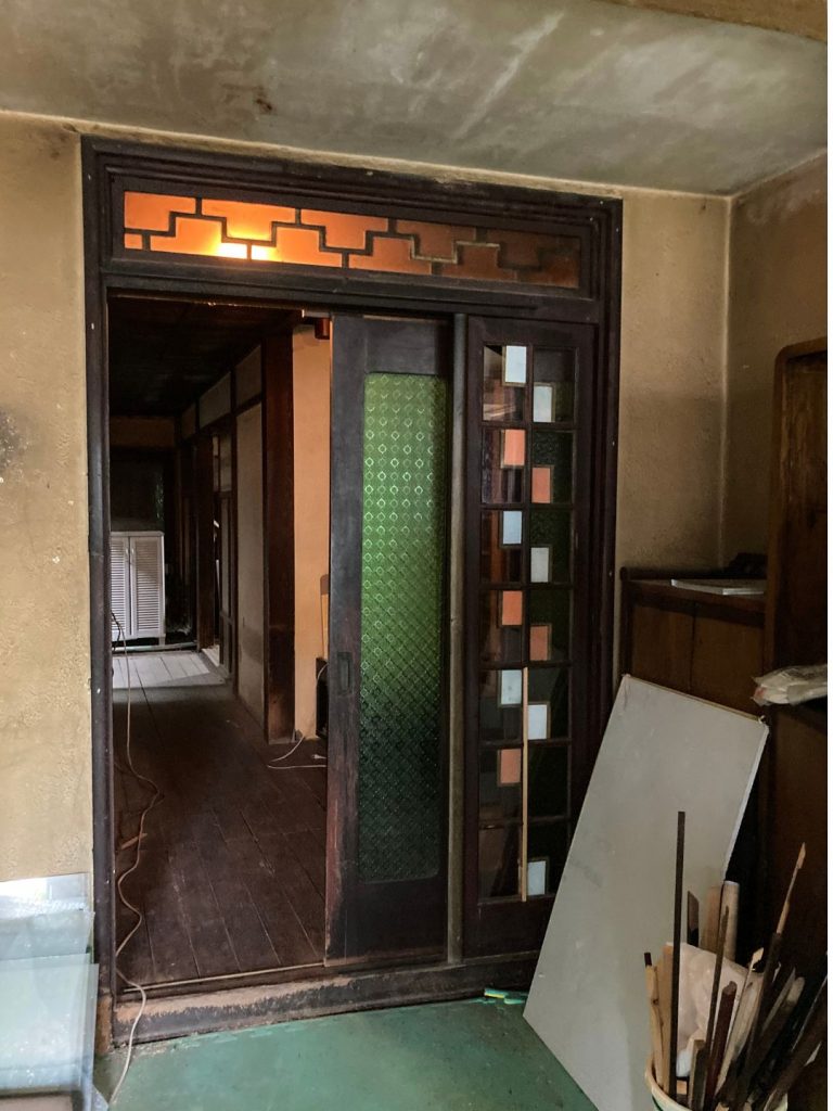 旧加島楼2階の廊下へ続く入り口。模様入りのすりガラスと色ガラスを組み合わせた引き戸越しに、奥へ長く伸びる木の廊下が見えている様子。