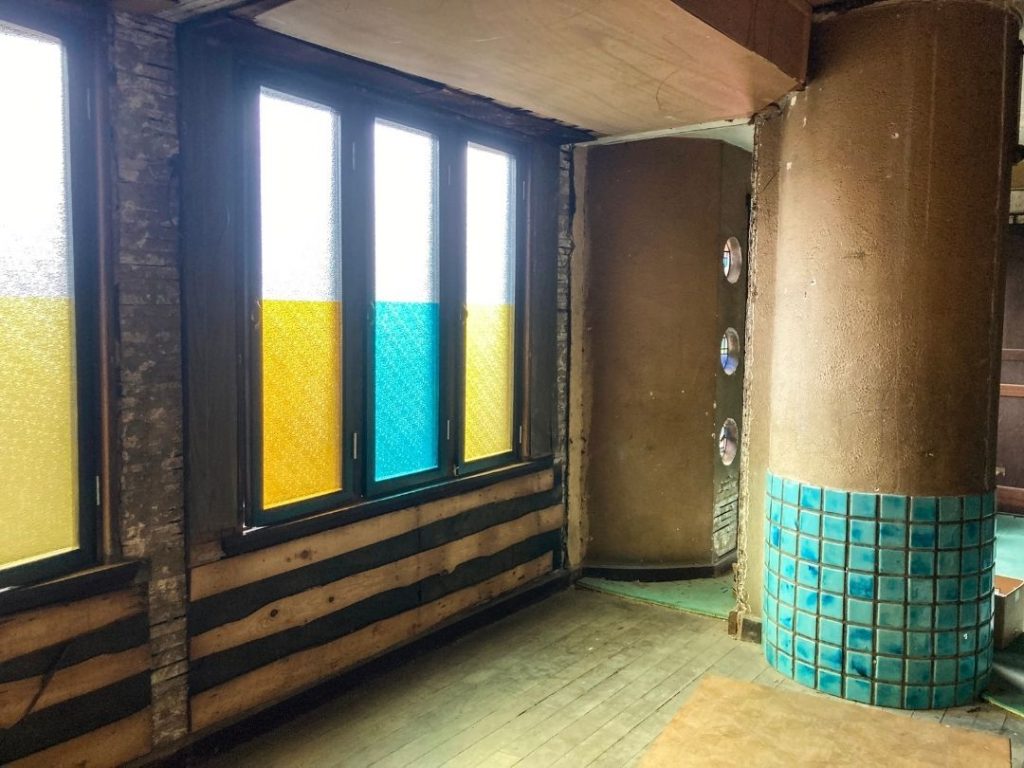 旧加島楼2階、黄色と水色の色ガラスがはめ込まれた窓と、円柱の下部に貼られた青緑色タイルが特徴的な室内の一角。