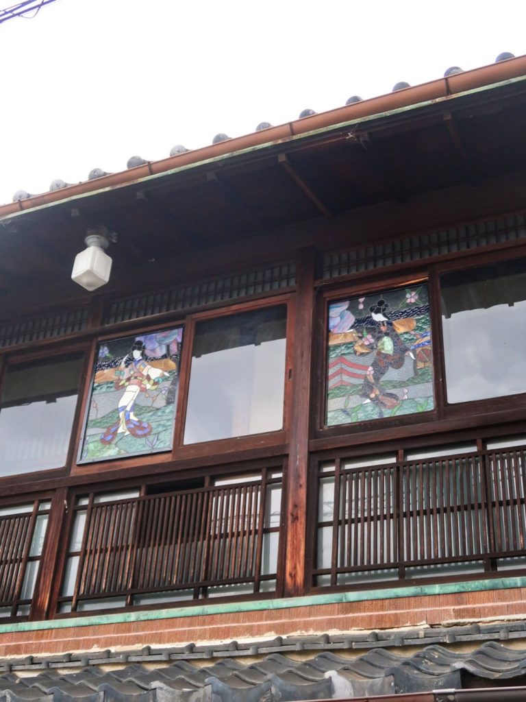 旧加島楼の外観。2階の窓に、着物姿の人物が描かれたステンドグラスが2枚並んでいる様子。