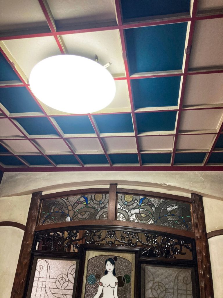 旧加島楼の天井に残る格子状の化粧天井と、下部に配置された女性像のステンドグラス装飾。
