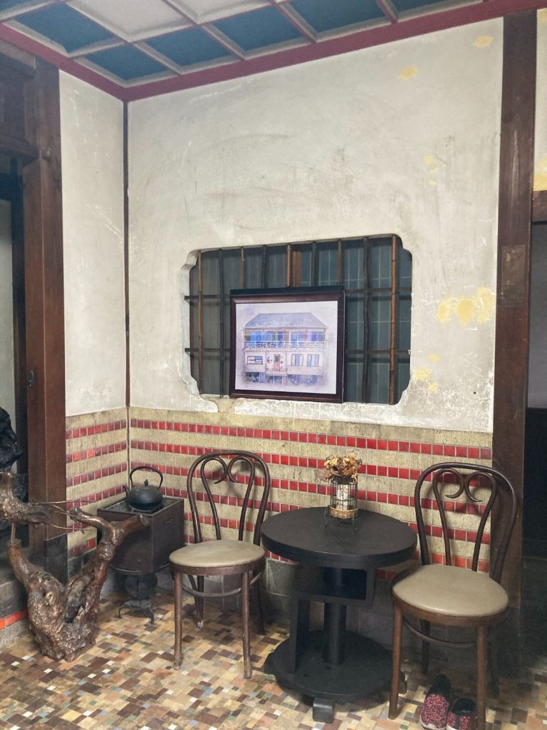 旧加島楼の一角に残るタイル壁とモザイク床、剥離した壁面に飾られた建物の絵、丸椅子と丸テーブルが置かれたレトロな空間。