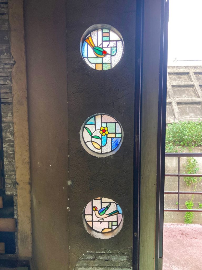 旧加島楼2階、鳥や花のモチーフが描かれた円形ステンドグラスが縦に3枚並ぶ壁面の装飾。