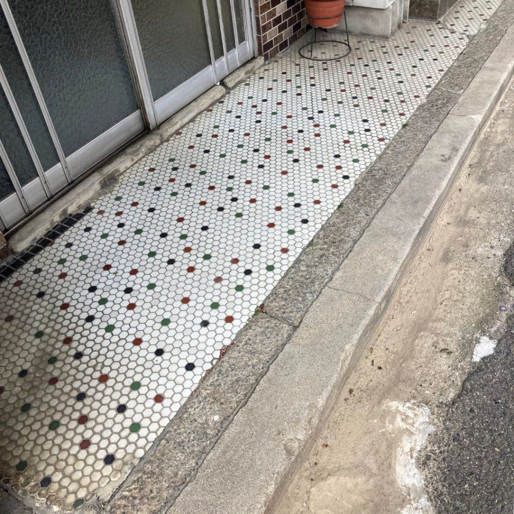 京都の軒先に残る白地の六角形タイル床。赤・緑・黒などの小さなドットが規則的にアクセントを添えるレトロなデザイン。