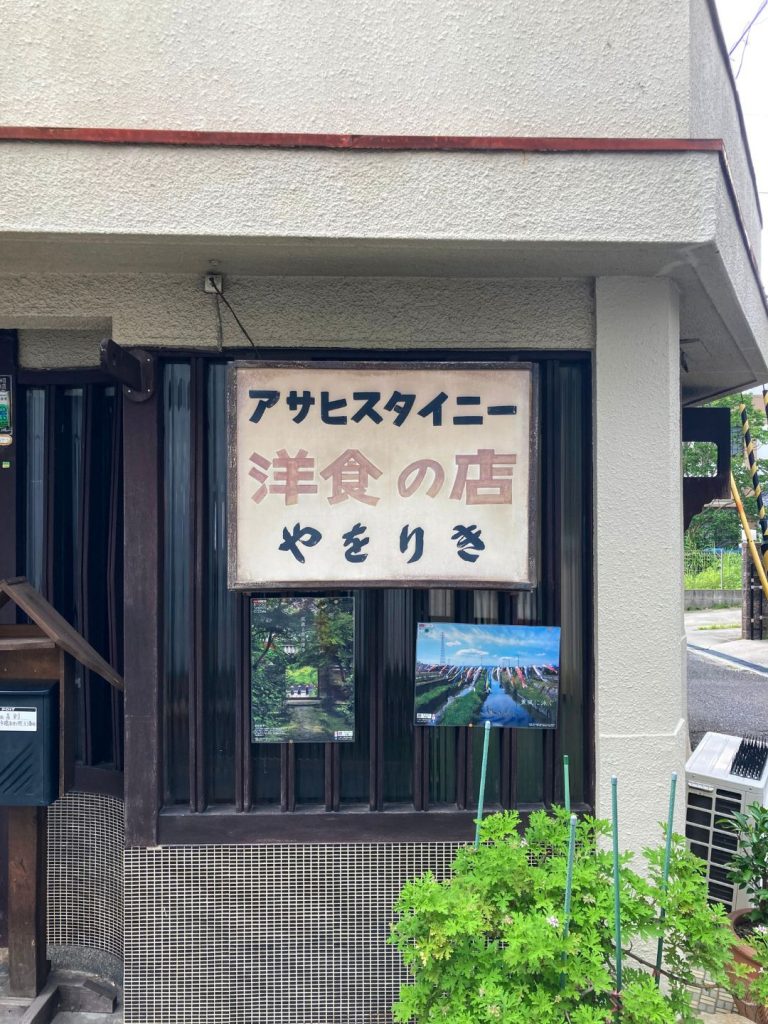 洋食店やをりきの外観。白壁に掲げられた店名看板と、格子窓やタイル外壁がレトロな雰囲気を漂わせている。